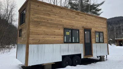 The exterior of a tiny house on wheels with wooden siding and a metal skirt.