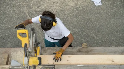 A student is photographed from above using a yellow chop saw to cut a piece of lumber. 