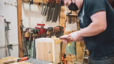 A student uses a pull saw to cut splines on a box. 