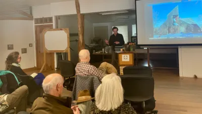 A speaker gestures at a presentation slide on a screen in a classroom.