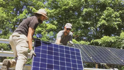 Two people lift a solar panel into place on a roof.