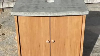 A douglas fir wood bathroom vanity cabinet with a gray concrete countertop with a drain opening to accomadate a vessel sink. 