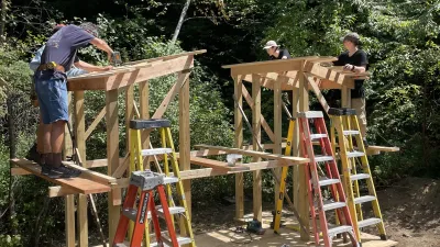 Students standing on a wooden platform adding the roof structure to a carpentry project.