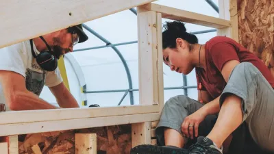 Two people look at a framed window opening of a tiny house