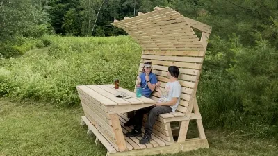 Two people sit on a picnic bench with an awning on a lawn