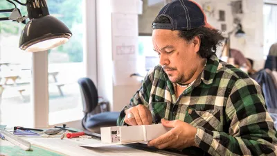 A student sitting at a drafting table and building an architectural model. 