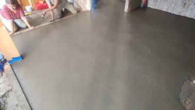 An earthen floor inside a strawbale building with two people finishing the last edge details.