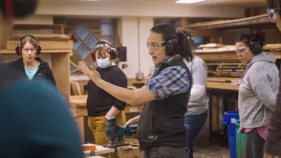 An instructor gestures in the woodshop in front of a group of students