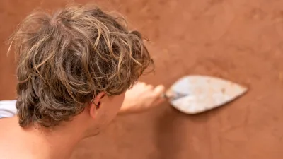 A student is photographed from behind plastering a wall with a trowel.