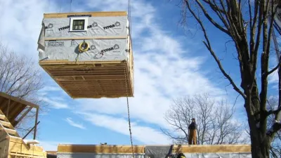 A module of a pre fabricated home wrapped in house wrap and suspended from a crane.