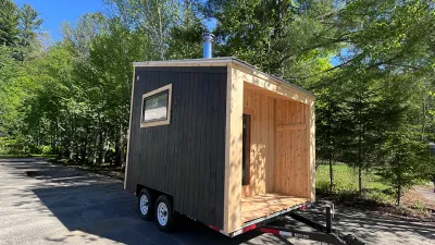 Exterior of a mobile sauna with dark siding and cedar trim. 