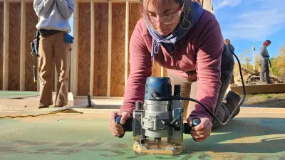 A semester student with a pink jacket and braid uses a router on the floor deck
