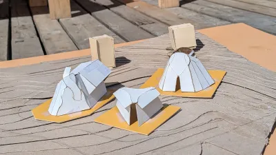 Several paper models are photographed outside on a wooden deck.