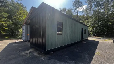 The exterior of a shipping container home clad in teal shiplap siding and black metal.