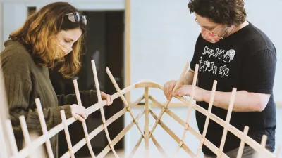 Two people work on lashing together ribs of a canoe frame.