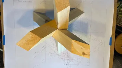 A wooden model of a three legged trestle set on top of hand drawn plans. 