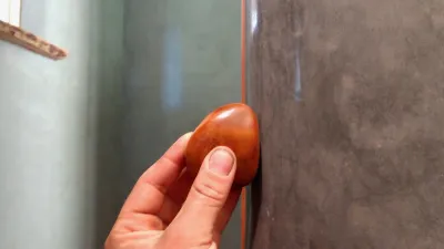 A close up shot of a hand using a red stone to burnish a gray plastered wall.