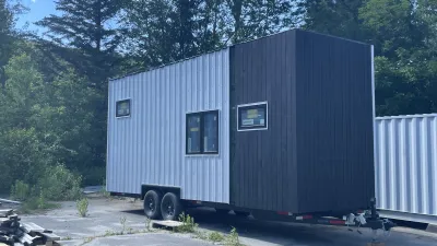 The backside of a tiny house on wheels with shed roof, a combination of silver metal and black board siding with several windows.