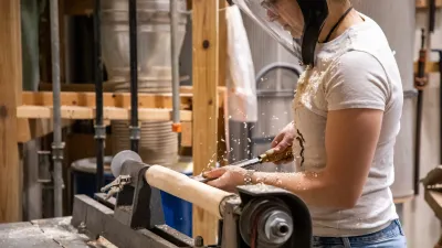 Close-up of a person woodturning on a lathe with wood shavings flying through the air.