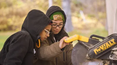 An instructor guides a student at a chop saw station in an outdoor classroom.
