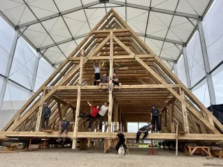 A group of carpenters poses in front of several-story-high trusses assembled in an indoor building space.