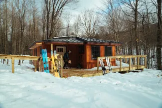 Wide shot of the Chittenden Brook Hut in winter with snow on the ground and skis outside.
