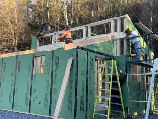 Several people working on a framed and partially zipped building