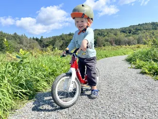 A young child rides a balance bike on a gravel path.