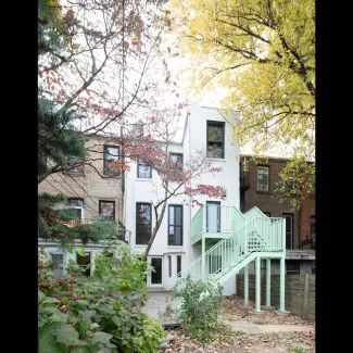 A renovated brownstone is photographed from the garden side on a sunny day