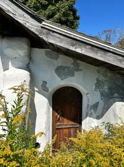 Close up shot of a strawbale building with arched doorway and slanted roofline. 
