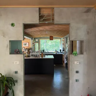 The interior living space of a Prickly Mountain home is shown, with crenellated concrete walls leading into the kitchen in the background.