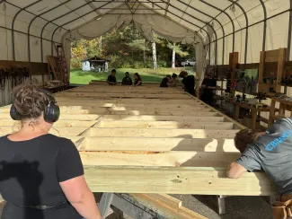 Floor deck complete! The semester students look on, it is a sunny day in the outdoor tent classroom..