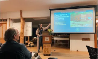A speaker gestures at a presentation slide on a screen in a classroom.
