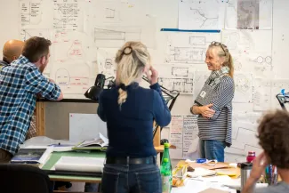 Students in the main studio gather around designs pinned to the wall, in active conversation.