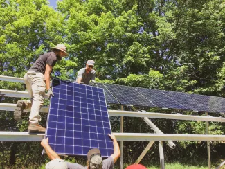 People lift a solar panel onto a roof for installation