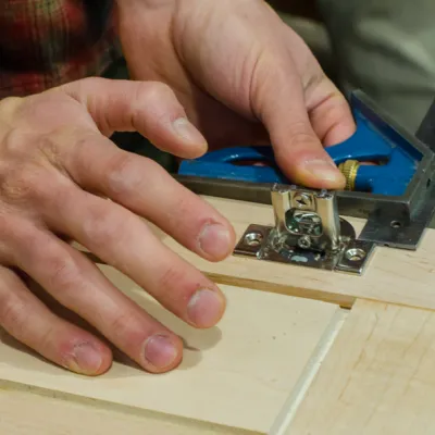 A close up of a pair of hands installing a cabinet hinge.