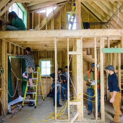Students installing electrical wiring inside a wood-framed house.