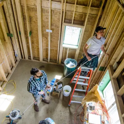 Two students running electrical wires inside a wood framed building.