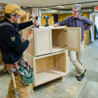 A instructor talking to students and standing next to a set of cabinets under construction.