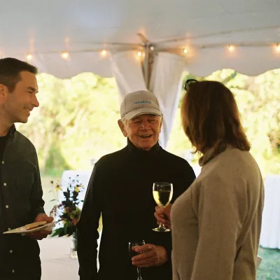 A group of three people mingle under a white tent.