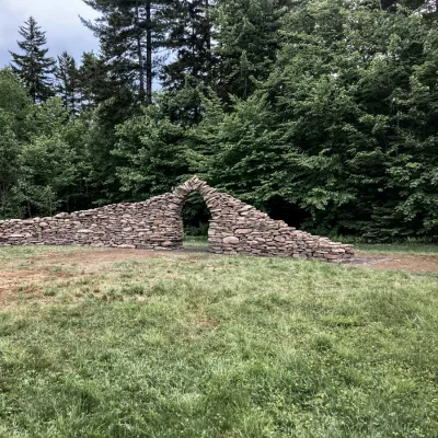 Gothic arch stone wall in a field with trees in the background.