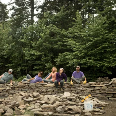 Five students posing on a partially completed stone wall.
