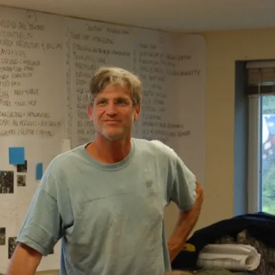 Bill stands in a classroom with a whiteboard behind him. He is looking up and to the left of the camera, wearing a light green tshirt.