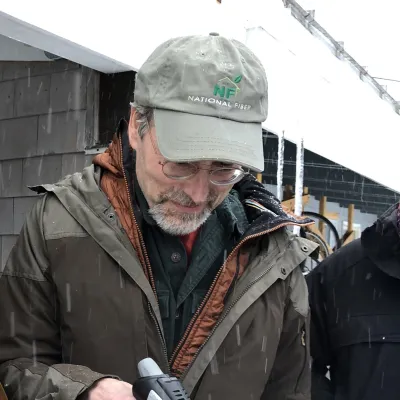 Bill stands outside in the winter, using a blowtorch to demonstrate insulation fire resistance.