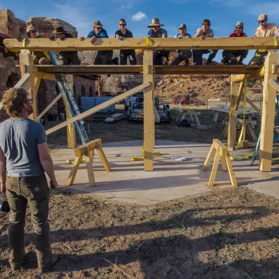 A long exposure shot of a timber frame being raised in the desert - bluffs in the background and very blue sky.