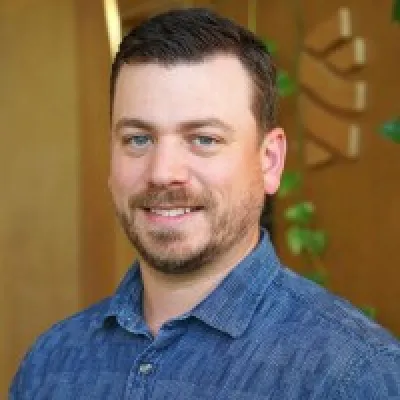 Branden smiles at the camera, headshot style. He has short brown hair and a blue collared shirt.