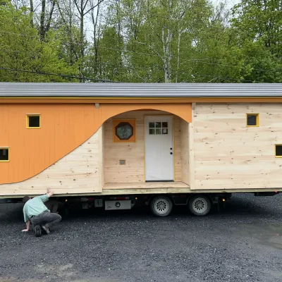 A bunkhouse building on a trailer. The building has a circus wagon style and orange details.