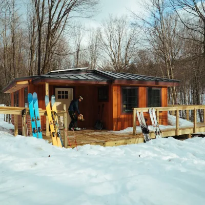 Wide shot of the Chittenden Brook Hut in winter with snow on the ground and skis outside.