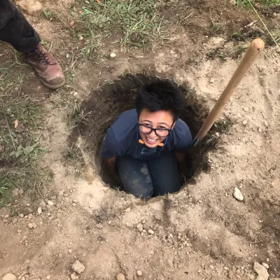 Chris looks up at the camera from a hole dug into the ground. 