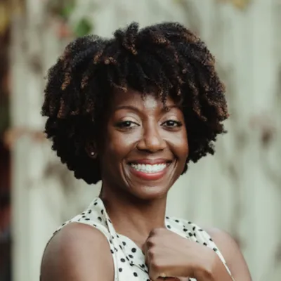 Desiree smiles at the camera, headshot style. She has black curls and is wearing a polka-dot top.
